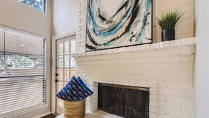 A room with a white brick fireplace, a large abstract painting, and a wicker basket with blue pillows. - Townhome Medical Ctr/Six Flags/La Cantera/Rim (San Antonio)