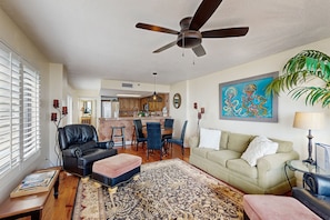 A spacious living room with a ceiling fan, a dining area, and a kitchen in the background.