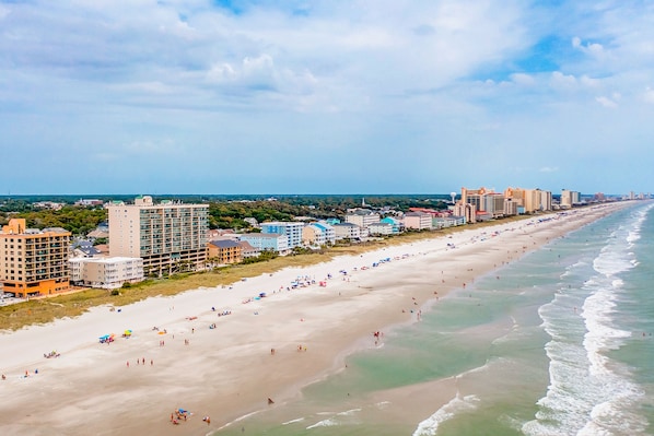 A coastal cityscape with a wide beach, high-rise hotels, and a clear sky.