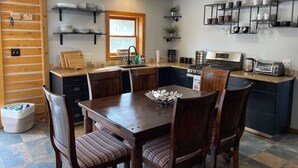 A kitchen with wooden cabinets, a dining table with chairs, and a coffee maker. - Cozy Mountain Cabin W/ Hot Tub Breathtaking Views (Alma)