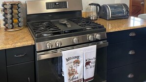 A kitchen with a stainless steel stove, a toaster, and a coffee machine on the counter. There are shelves above the counter holding mugs and glasses. - Cozy Mountain Cabin W/ Hot Tub Breathtaking Views (Alma)