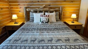 A cabin-style bedroom with a log wall headboard, two bedside lamps, and a bed with patterned bedding. - Cozy Mountain Cabin W/ Hot Tub Breathtaking Views (Alma)