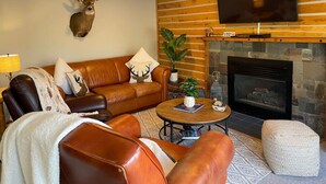 A living room with a leather sofa, a coffee table, a mounted deer head, a fireplace, and a flat-screen TV. - Cozy Mountain Cabin W/ Hot Tub Breathtaking Views (Alma)