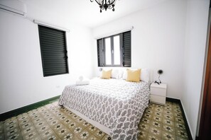 A bedroom with a bed, nightstand, and two windows with shutters. - Colonial Apartment with Generator, Free Parking, (San Juan)