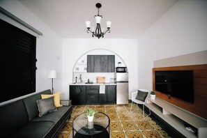 Un espace de vie compact comprenant un canapé, une table basse, un téléviseur, un coin cuisine et un sol à motifs.