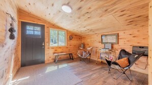 Un interior acogedor de cabaña con una puerta de madera, un banco, una silla plegable, una mesita y un televisor.