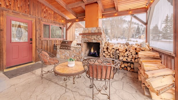 Interior acogedor de una cabaña con chimenea de piedra, paredes de madera y comedor con sillas de metal y una mesa redonda.