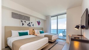 A hotel room with two beds, a desk, and a large window offering a view of the sea.