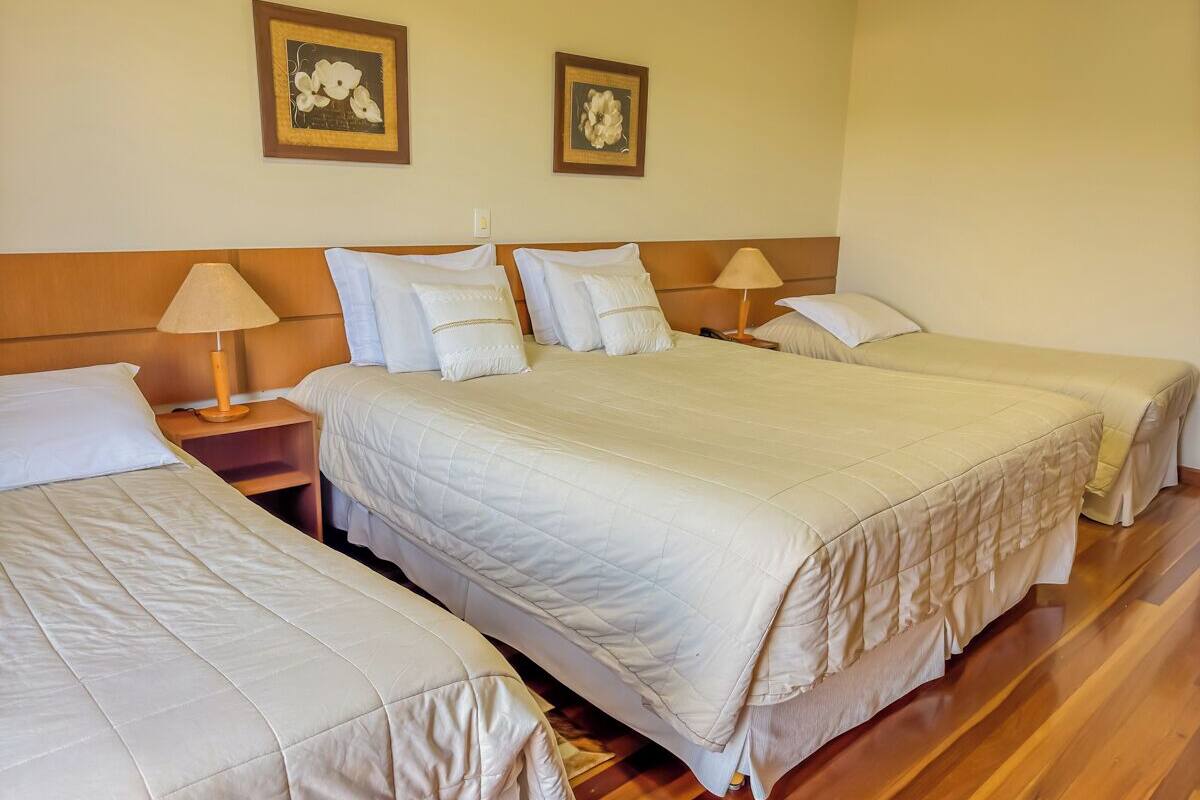 Habitación de hotel con tres camas, cabeceros de madera y dos lámparas fijadas a la pared.