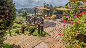 A wooden deck with outdoor furniture, surrounded by greenery and flowers. - Pousada Victoria Villa Campos do Jordão (Campos do Jordão)