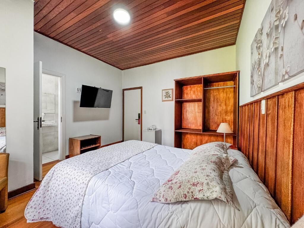 Un dormitorio con una cama grande, techo de madera, televisor montado en la pared y un armario de madera.