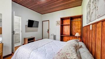 Un dormitorio con una cama grande, techo de madera, televisor montado en la pared y un armario de madera.