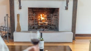 A fireplace with a burning fire, a bottle of wine, and a broom on a wooden table. - Pousada Victoria Villa Campos do Jordão (Campos do Jordão)
