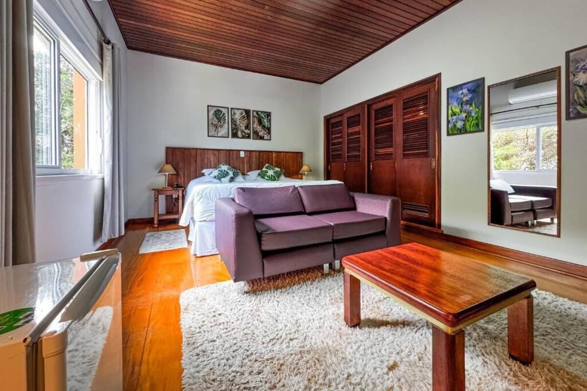 Una habitación con techo de madera, una cama con cabecera blanca, un sofá morado, una mesa de centro de madera y una alfombra blanca y mullida.