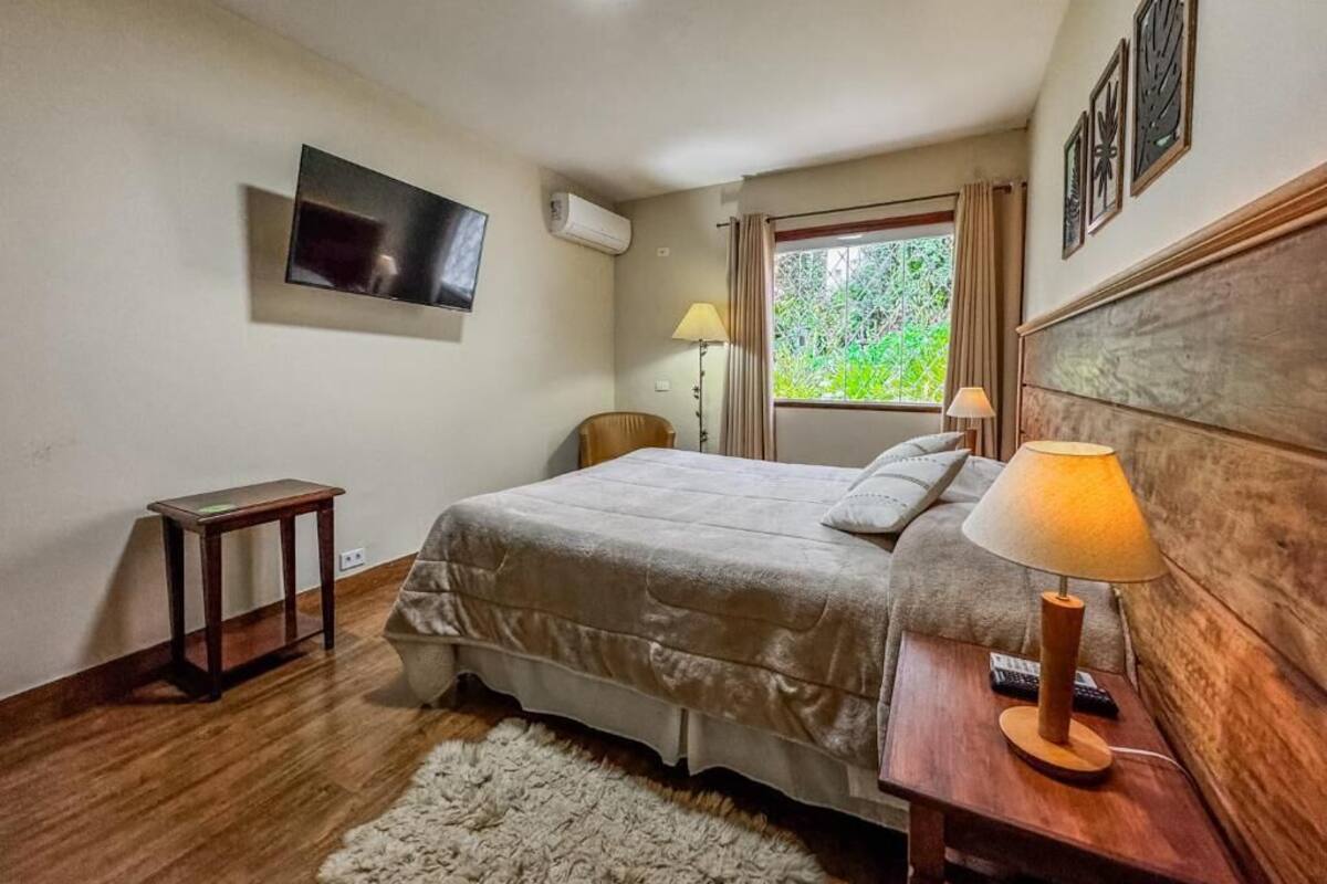 Un dormitorio con cama, lámparas de noche, un televisor montado en la pared y una ventana con cortinas.