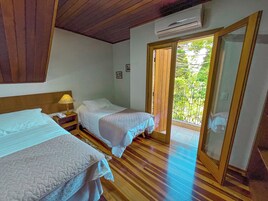 Una stanza con due letti, pavimento in legno, climatizzatore e un balcone con vista sul verde.