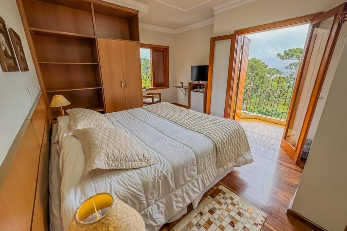 Un dormitorio con cama, armario de madera, televisor y balcón con vistas.