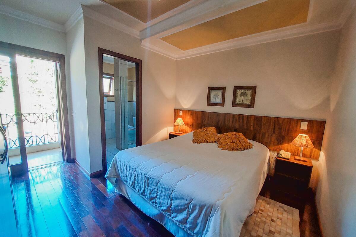 Un dormitorio con una cama grande, dos lámparas de noche, un cabecero de madera y vistas al baño a través de una puerta de cristal.