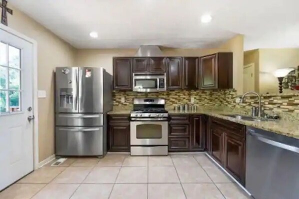 Kitchen features a refrigerator, microwave, and oven, with dark cabinets and a granite countertop.