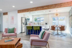 Una cocina moderna con armarios blancos, un refrigerador de acero inoxidable y una isla azul. Hay un comedor con una mesa de vidrio y sillas.