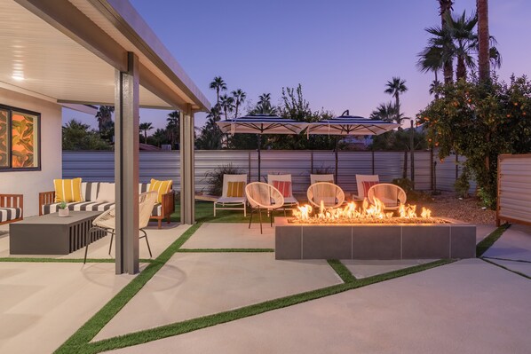 Un patio al aire libre con una chimenea, asientos y una zona cubierta con sombrillas.