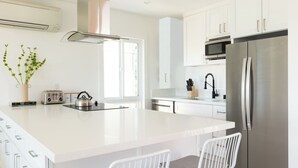 Una cucina moderna con mobili bianchi, un frigorifero in acciaio inossidabile, un forno a microonde integrato e una grande isola con bollitore e tostapane.
