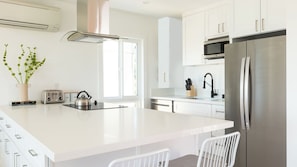 Une cuisine moderne avec des meubles blancs, un réfrigérateur en acier inoxydable, un four à micro-ondes encastré et un grand îlot central doté d’une bouilloire et d’un grille-pain.