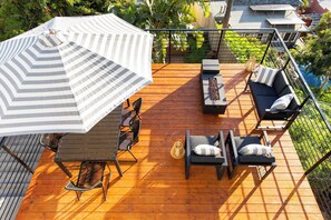 A wooden deck with a striped umbrella, outdoor furniture, and a view of a garden. - Avalon III by Avantstay Mins to Gaslamp, Zoo & Airport Beautiful Deck w/ BBQ (San Diego)