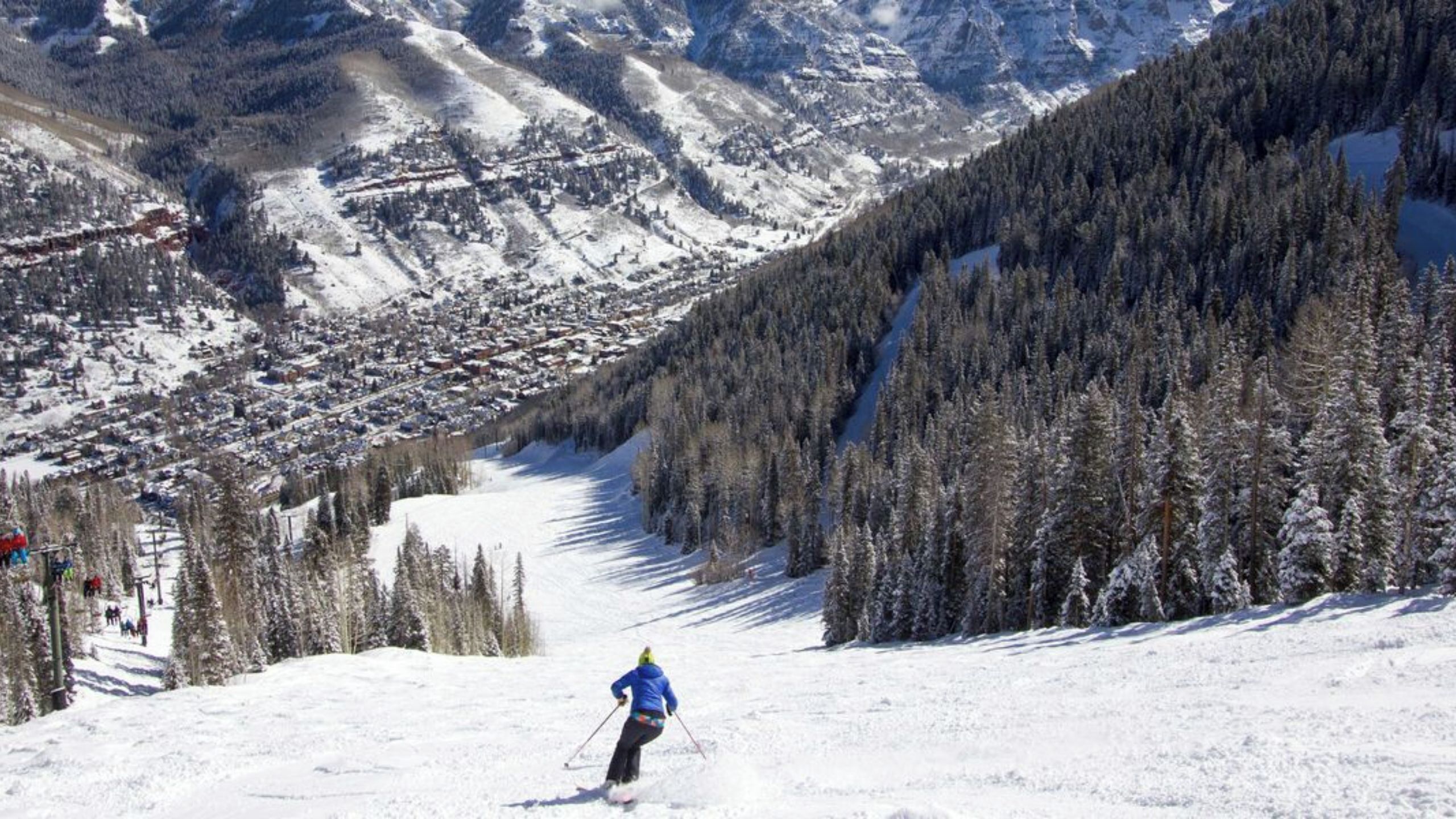 A ski slope with a skier, snow-covered trees, and a mountainous backdrop.