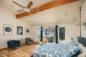 A bedroom with a bed, a chair, a ceiling fan, and a view through a glass door.