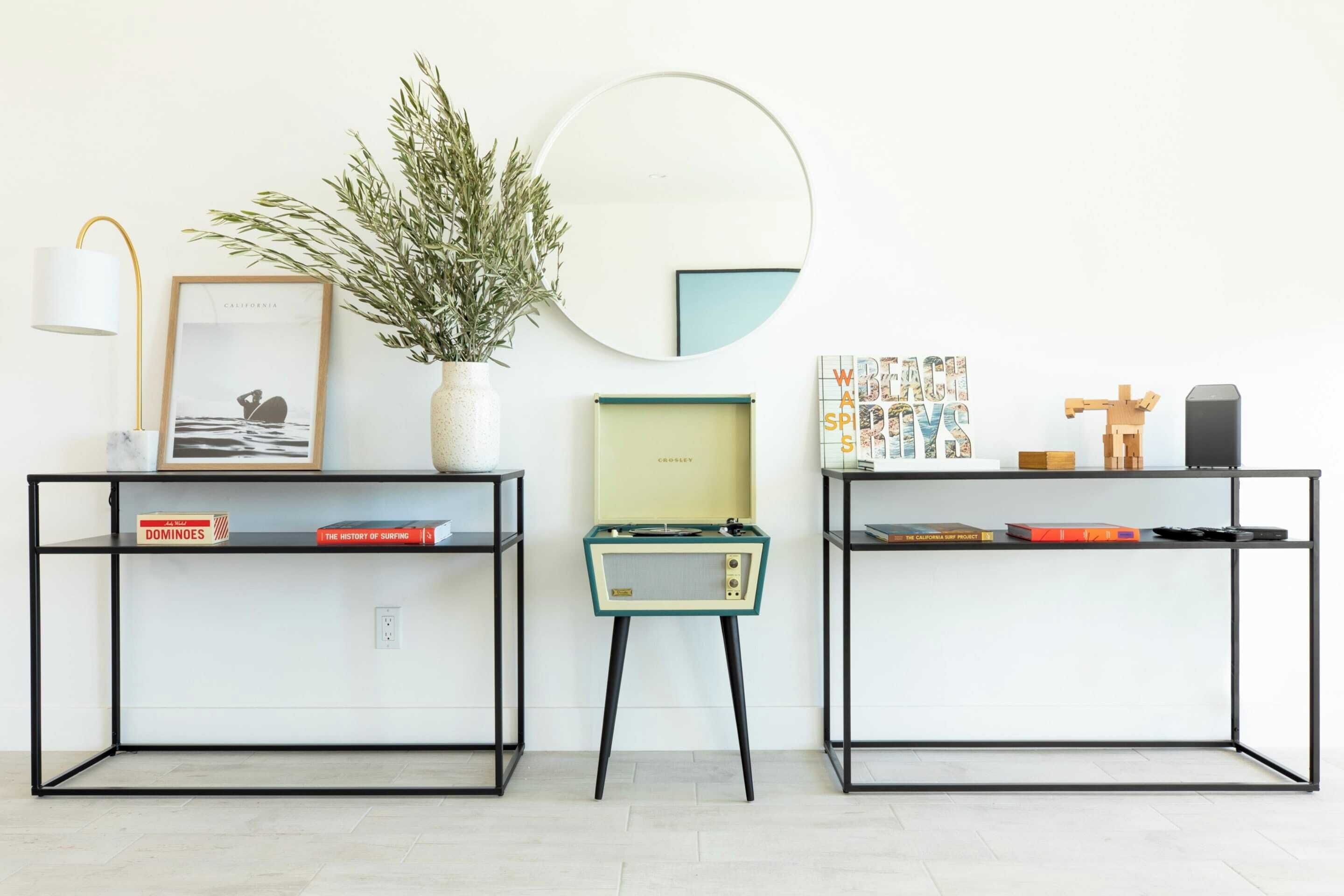 Two black metal desks with shelves, a small plant, a framed picture, a mirror, and a few books.