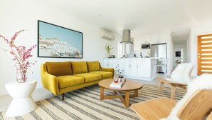 A modern living room with a yellow sofa, a round coffee table, and a kitchen area with white cabinets and stainless steel appliances. - Avalon I by AvantStay Contemporary San Diego Condo w Large Balcony (San Diego)