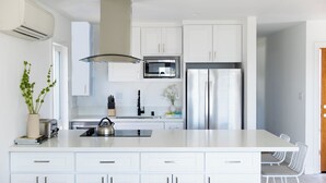 A modern kitchen with white cabinetry, a stainless steel refrigerator, a microwave, and a kettle on the island. - Avalon I by AvantStay Contemporary San Diego Condo w Large Balcony (San Diego)