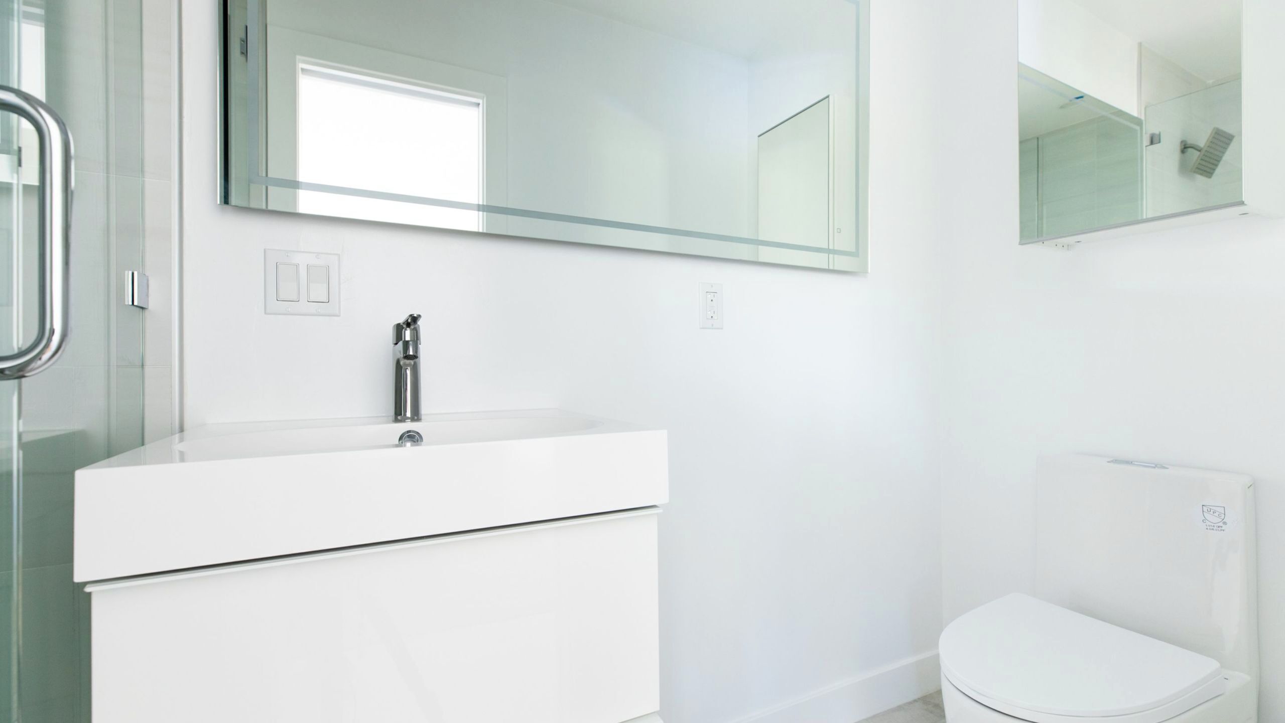 Un baño moderno con un tocador blanco, un espejo y un inodoro.