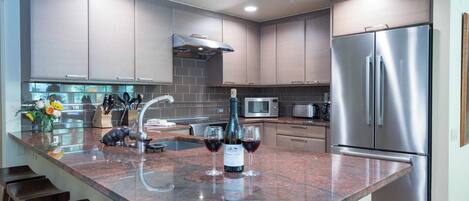 A modern kitchen with granite countertops, stainless steel appliances, and a wine bottle on the island.