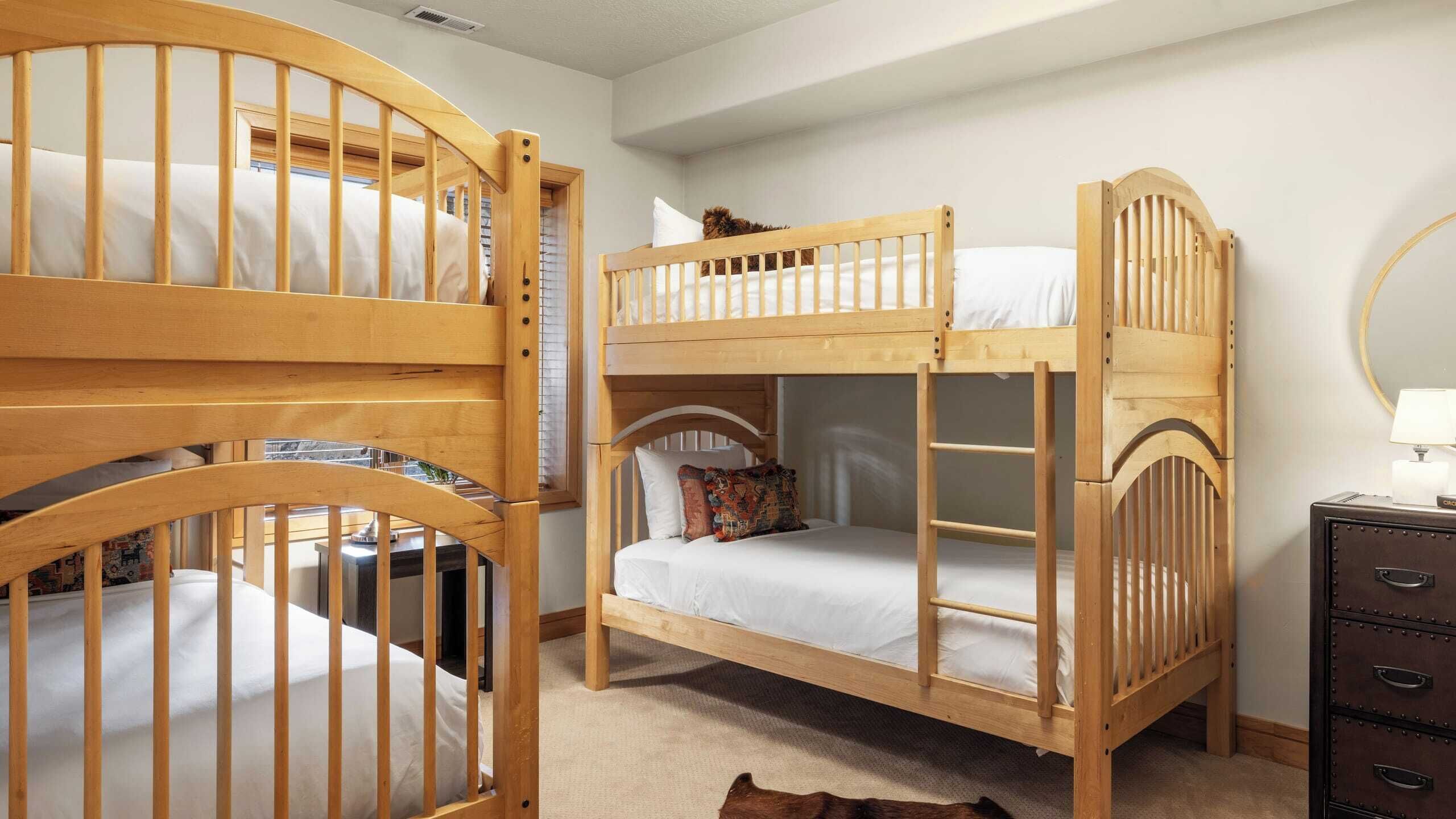 A room with two wooden bunk beds, a small desk, a dresser, and a mirror on the wall.