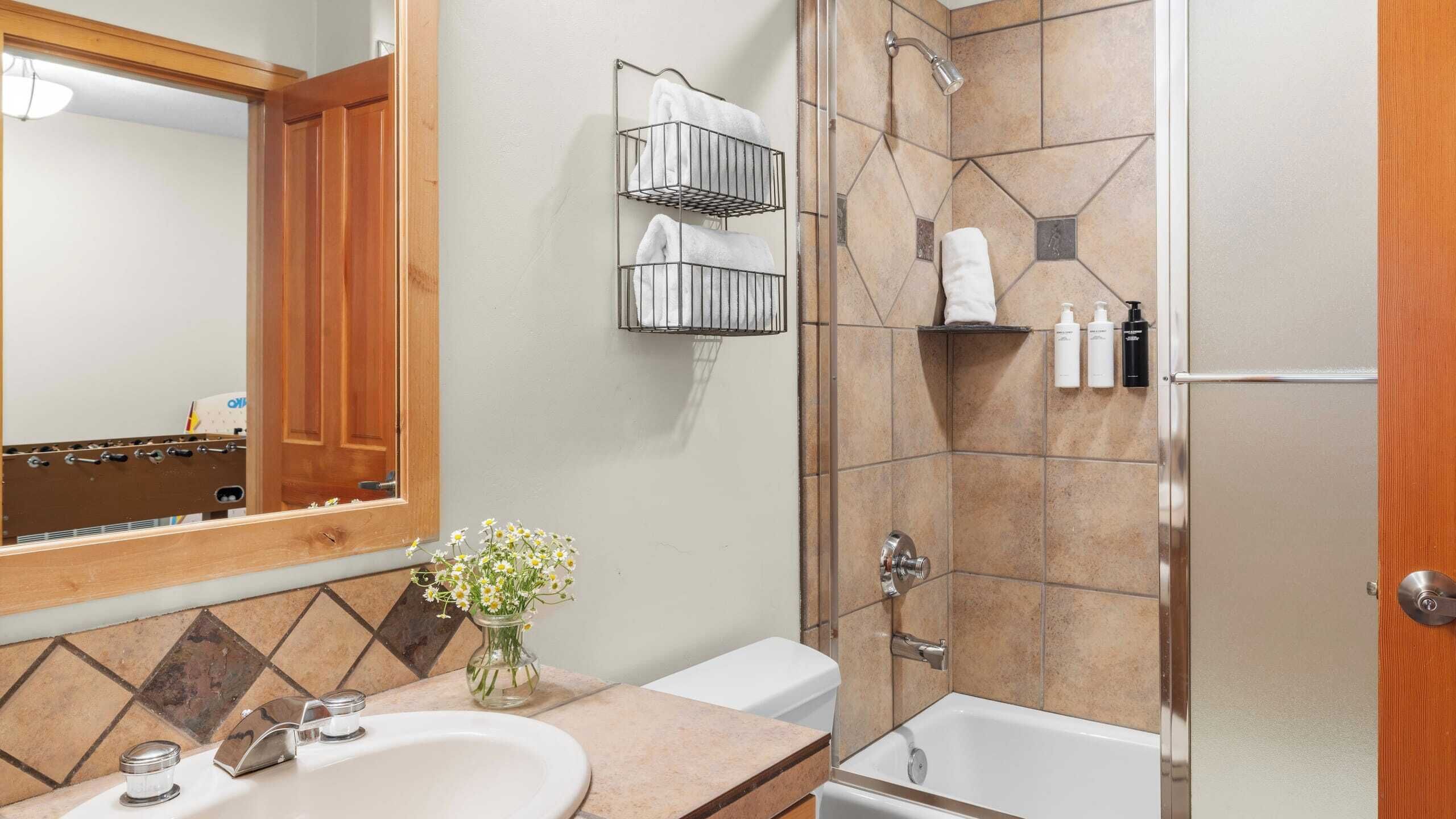 A bathroom with a wooden vanity, a sink, a mirror, a shower with a glass door, and a towel rack.