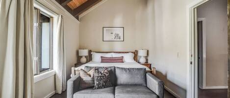 Una camera da letto con un letto, due abat-jour, un quadro appeso al muro e un divano grigio.