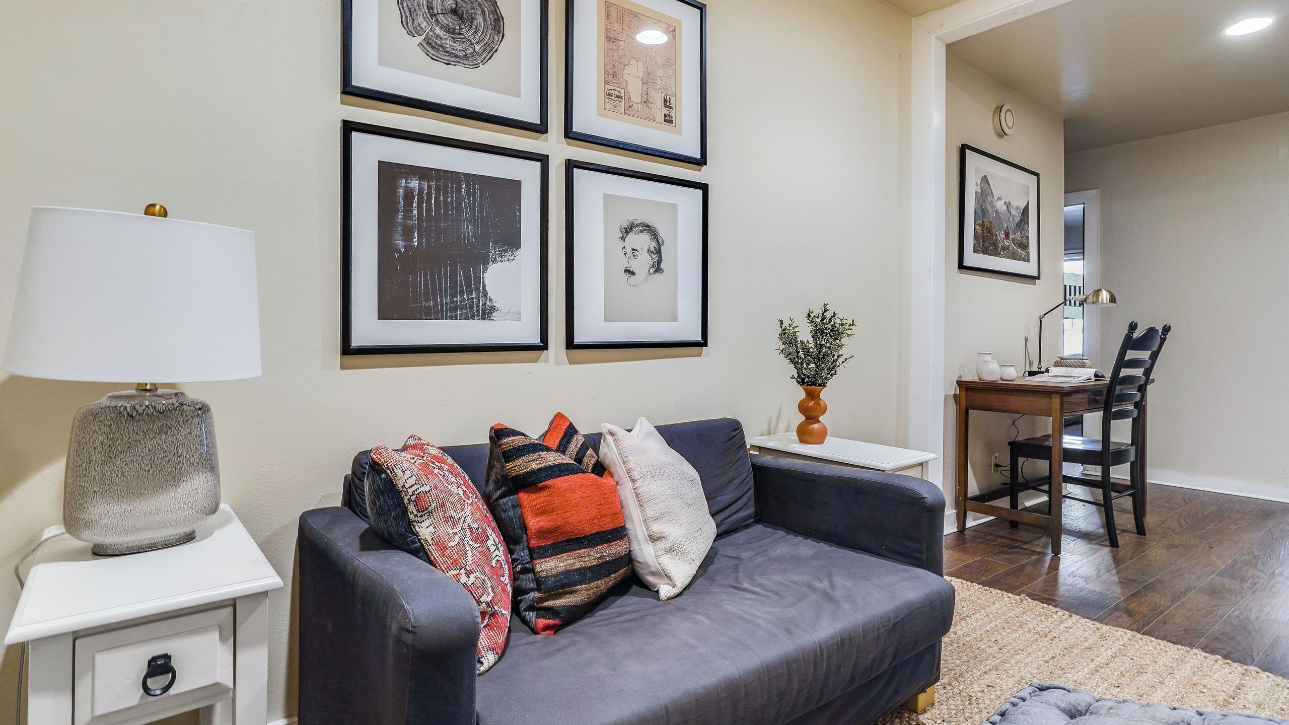 A living room with a dark grey sofa, a white side table, a lamp, and framed artwork on the wall.