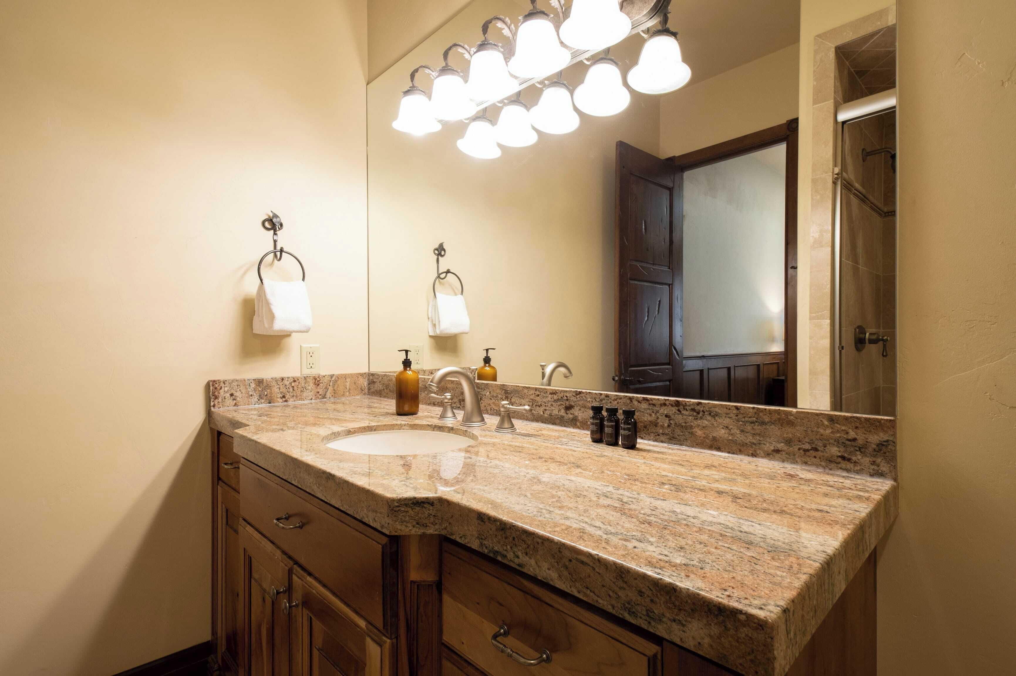 A bathroom with a granite countertop, a sink, a mirror, and a shower door.