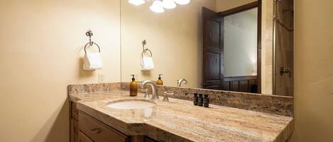 A bathroom with a granite countertop, a sink, a mirror, and a shower door.