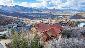 A mountain lodge with a red roof, surrounded by trees and a view of snow-capped mountains.