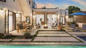 A modern outdoor patio with a pool, seating areas, and a well-lit interior space. - Vista Del Mar by Avantstay Stunning Spanish Inspired Home w/ Pool, Hot Tub & Rooftop Patio (La Jolla)