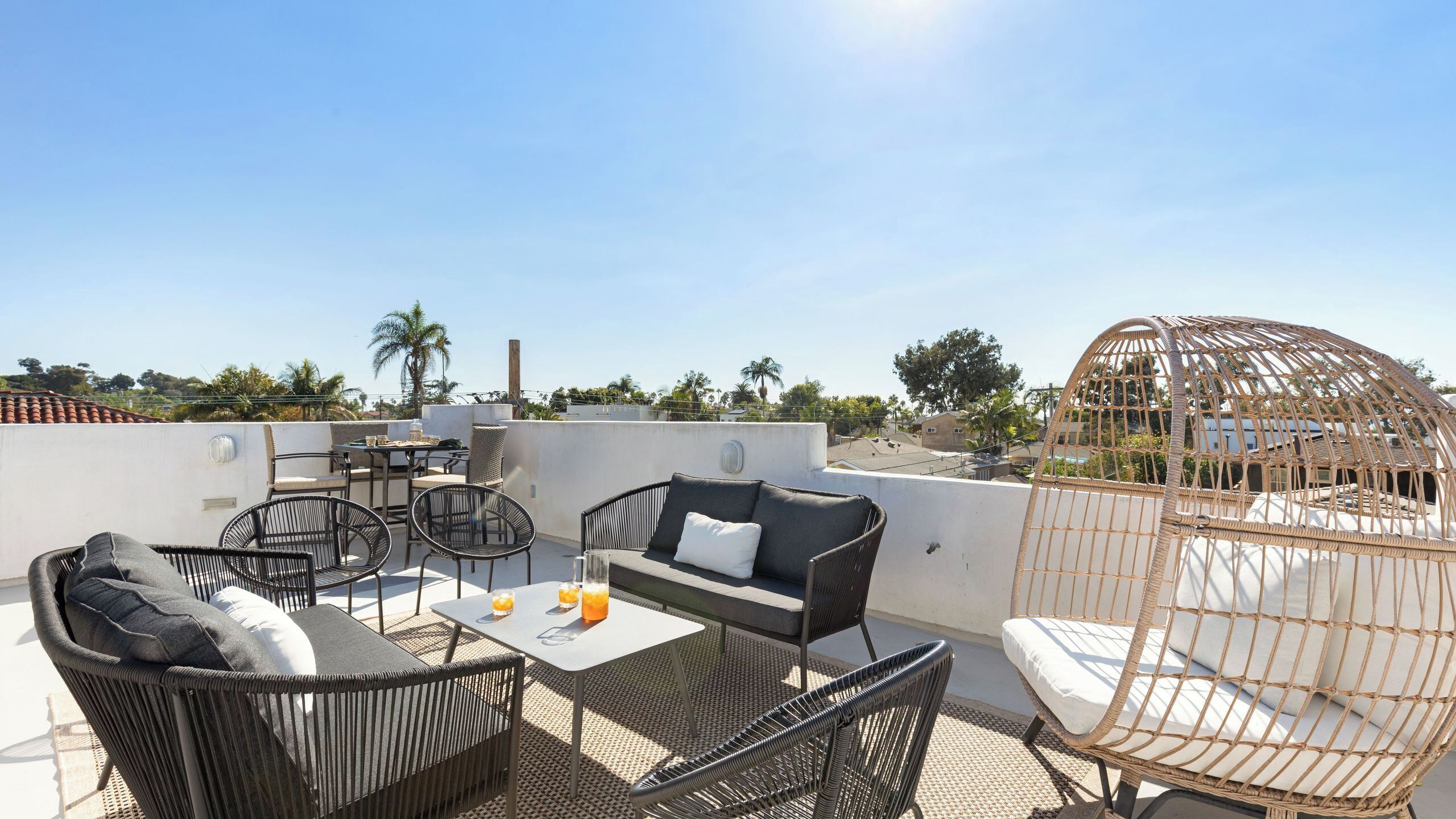 A rooftop patio with wicker furniture, a hanging chair, and a table with drinks.