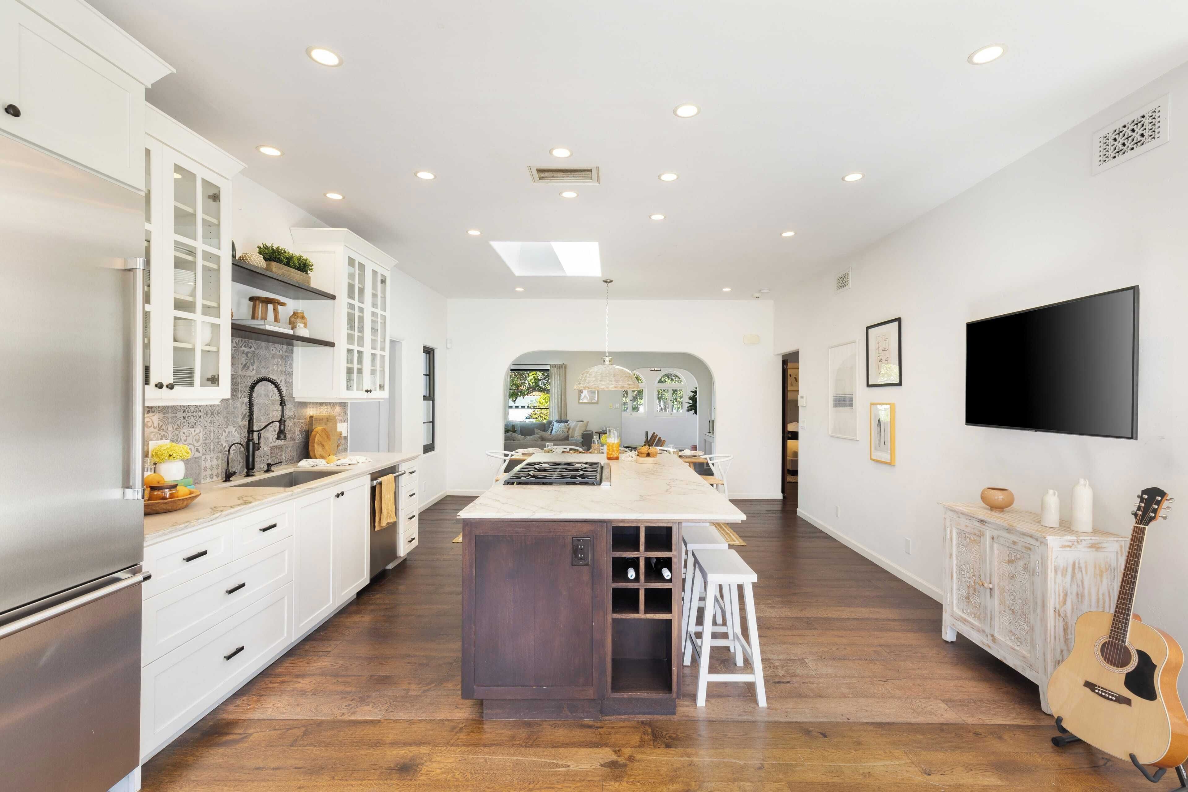 Una cocina moderna con armarios blancos, una isla central y un comedor con un televisor grande.