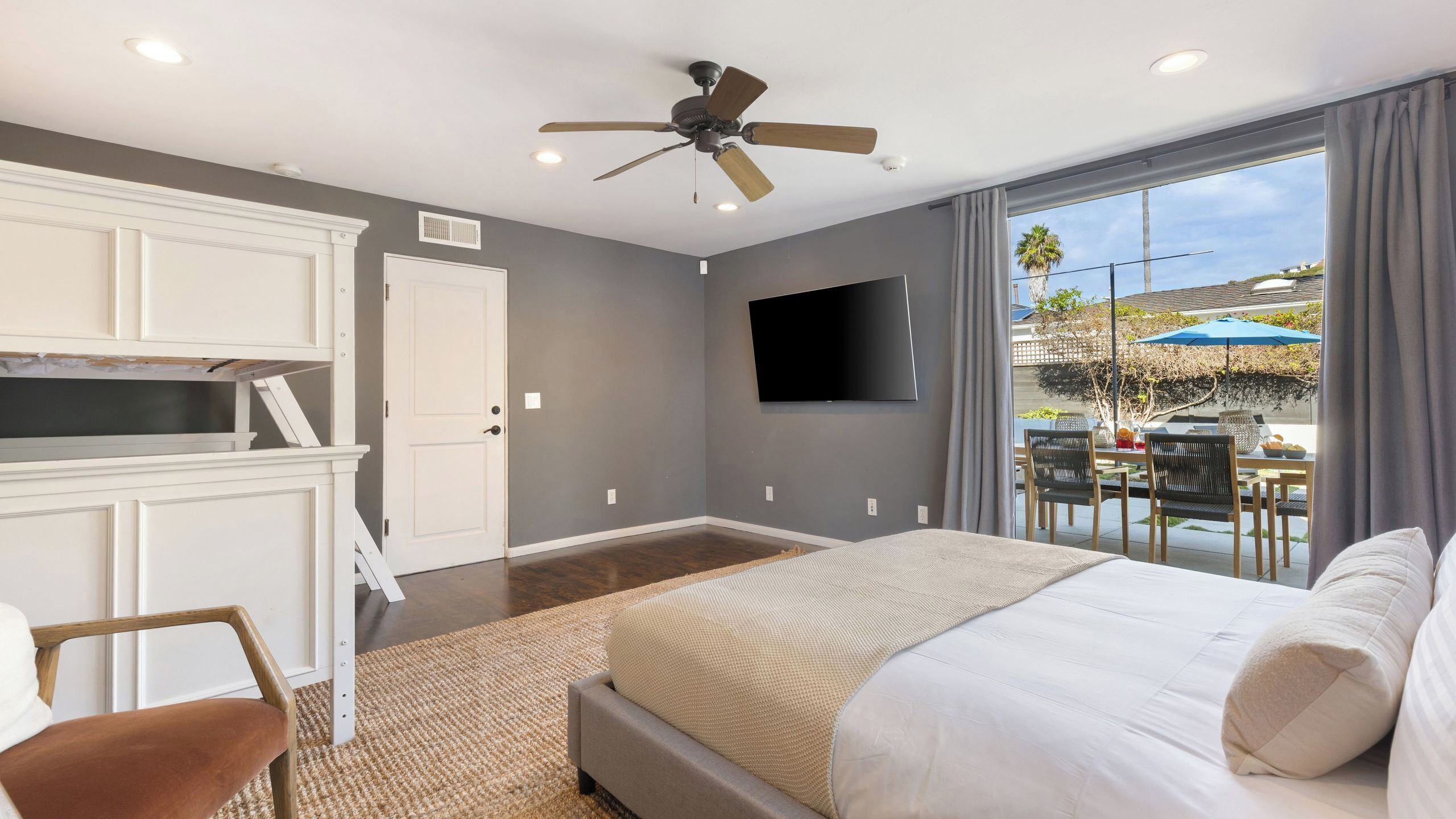 A bedroom with a bed, a TV, a ceiling fan, and a view of the outdoors.