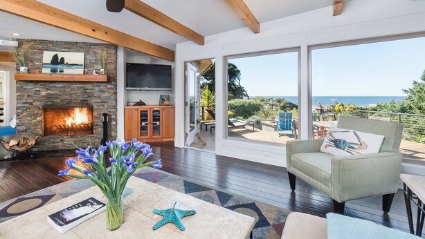A spacious living room with a fireplace, large windows, and a view of the ocean. - Rancho del Mar by Avantstay One Block From Beach (Arch Cape)