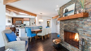 A cozy living room with a fireplace, a dining area, and a kitchen in the background. - Rancho del Mar by Avantstay One Block From Beach (Arch Cape)