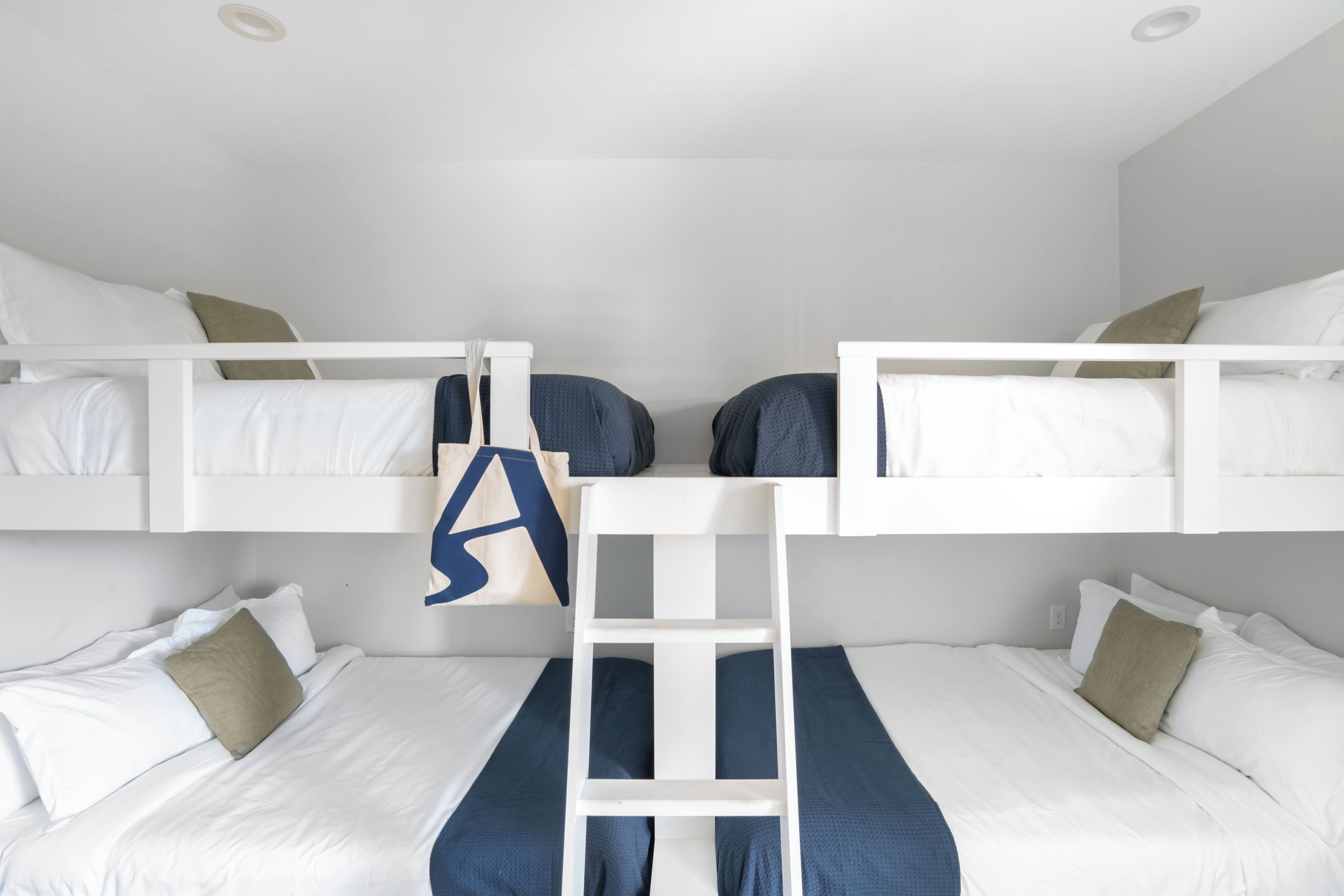 Een slaapkamer met stapelbed, witte beddengoed, een ladder en een blauwe handdoek.