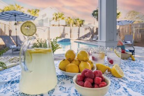 Un'area piscina con una brocca di limonata, ciotole di limoni e lamponi, e una piscina sullo sfondo.